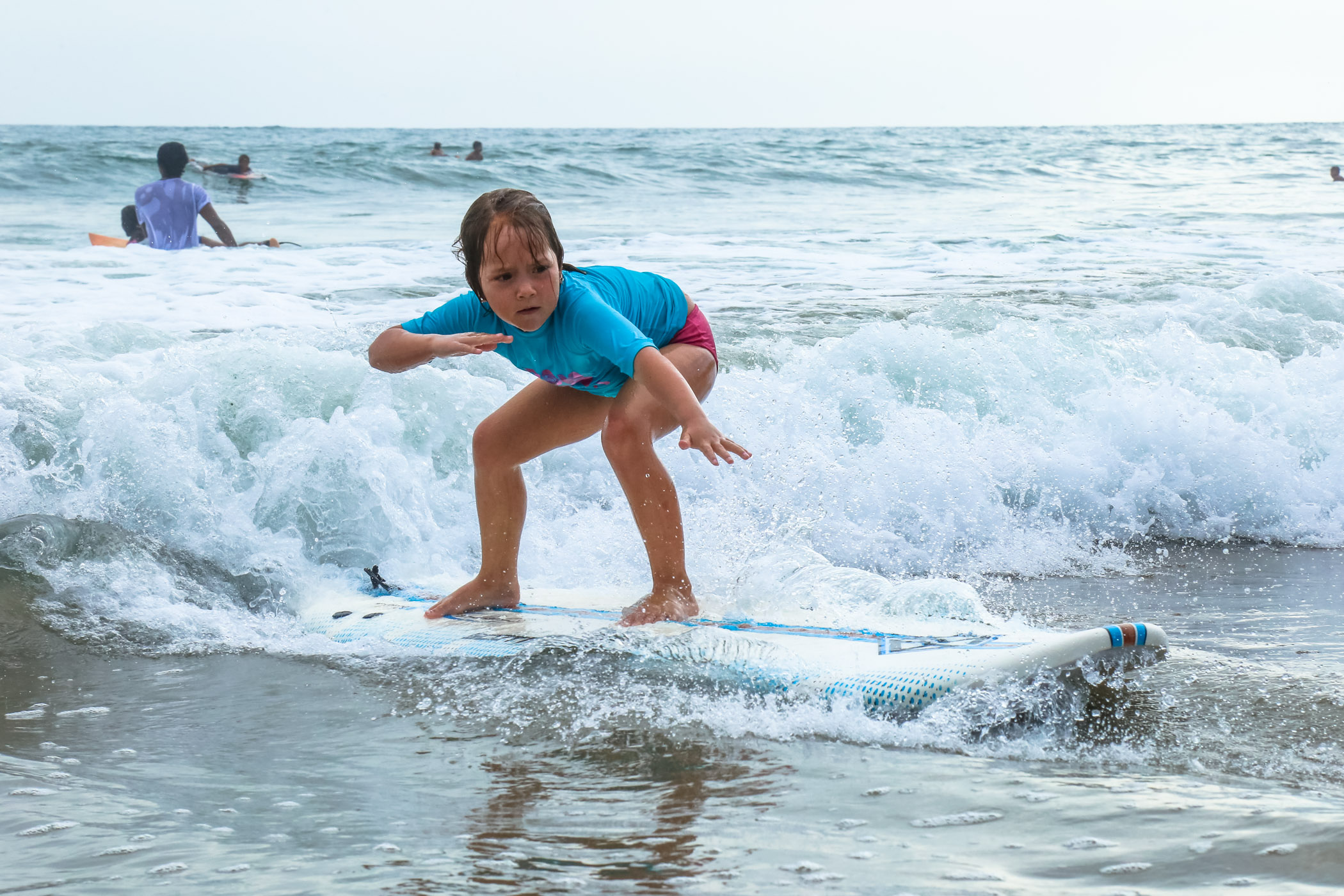 Close up of young Ecuadorian girl riding a wave into shore